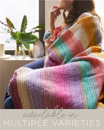 A woman sitting inside wrapped in a rainbow crochet blanket.