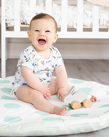 Baby playing with wooden push toy on plush play mat
