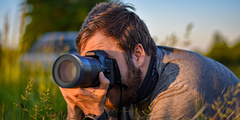 A man lays in the grass photographing minute details with Opteka's 10x Macro lens add-on.