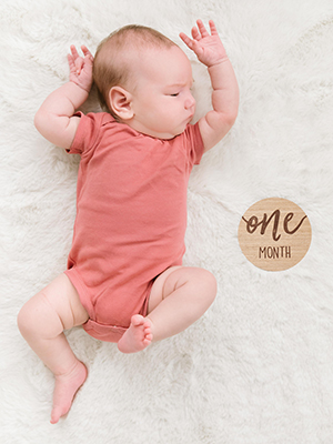 Newborn laying next to One Month milestone card